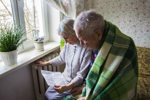 Elderly couple wrapped in blankets near a cold radiator